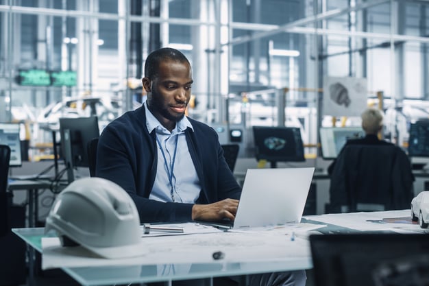 Man in business attire working on a laptop at a smart factory. 