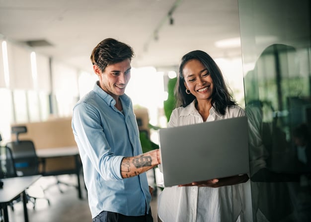 Two coworkers smiling working on a laptop
