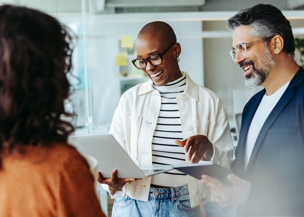 Three team members discuss an ongoing project with their laptops open.