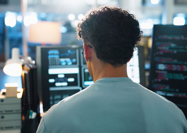 A software engineer facing away from the camera debugs code.