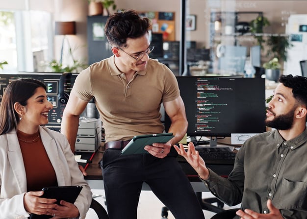 A small devops team collaborates on a project with lines of code displayed on their monitors.
