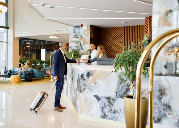 A guest with a suitcase interacting with front desk employees at a hotel.